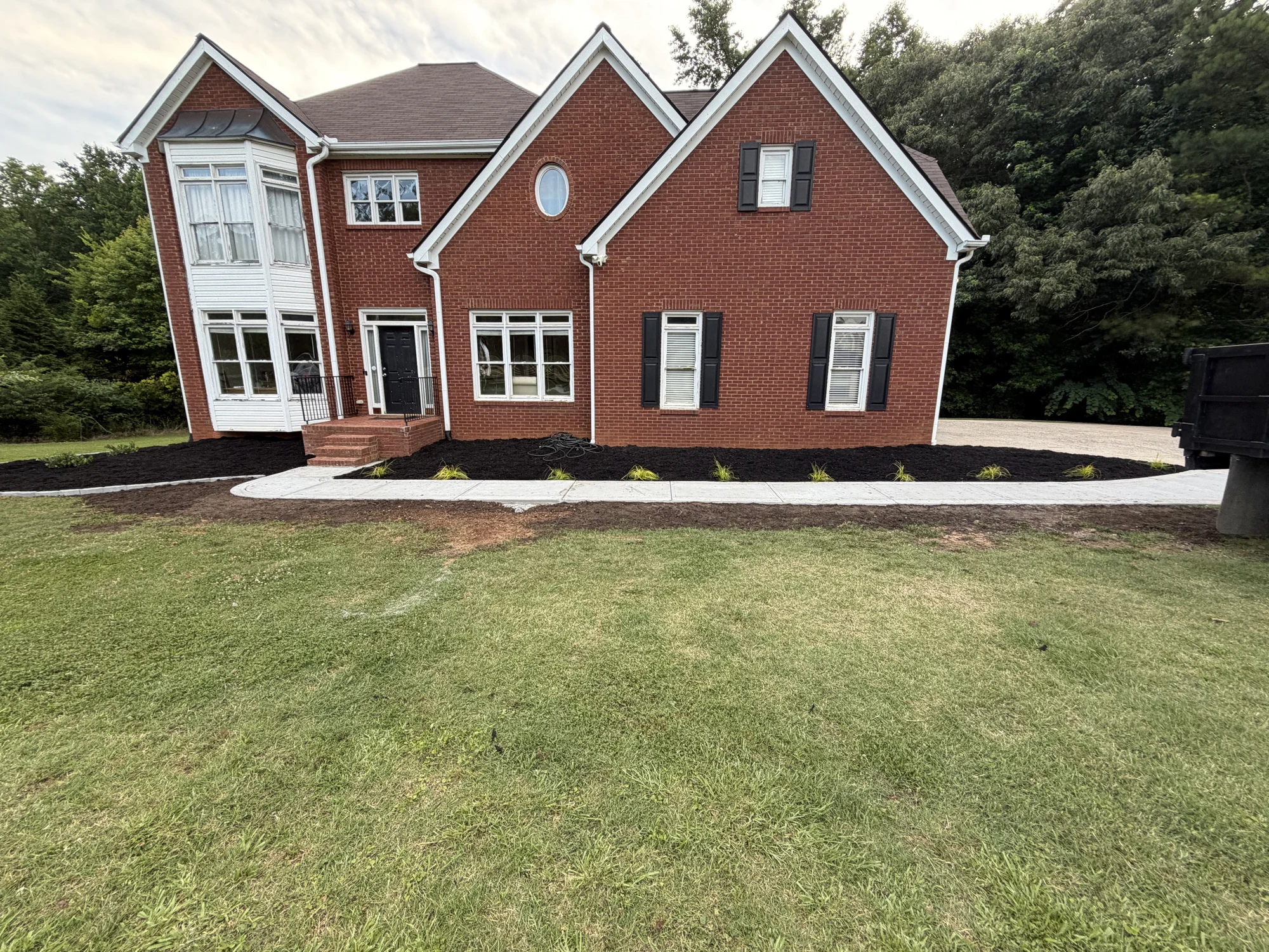 Brick home with a green lawn, fresh planting beds, and a finished concrete walkway